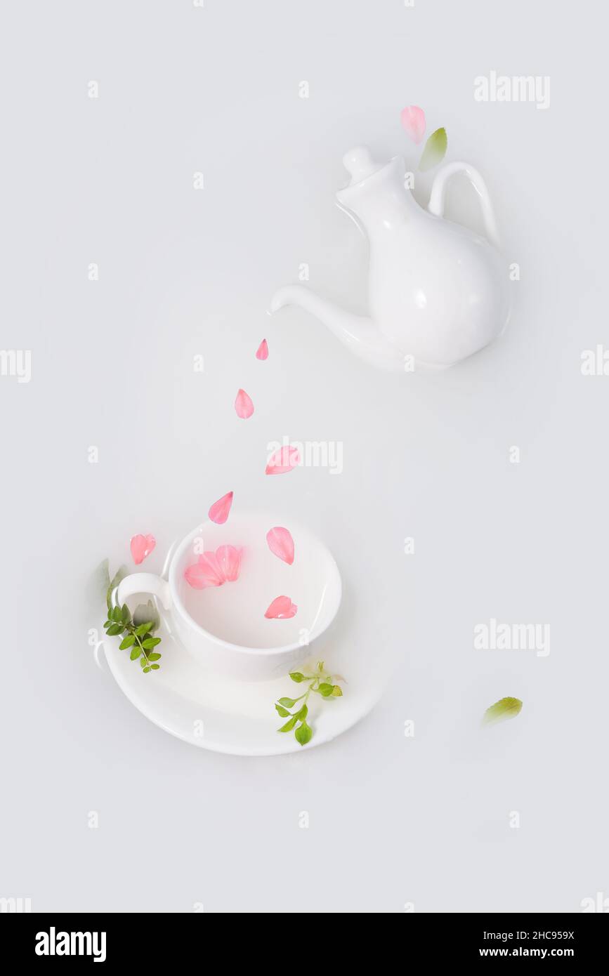 Pink petals drip from white porcelain teapot into cup. Stock Photo