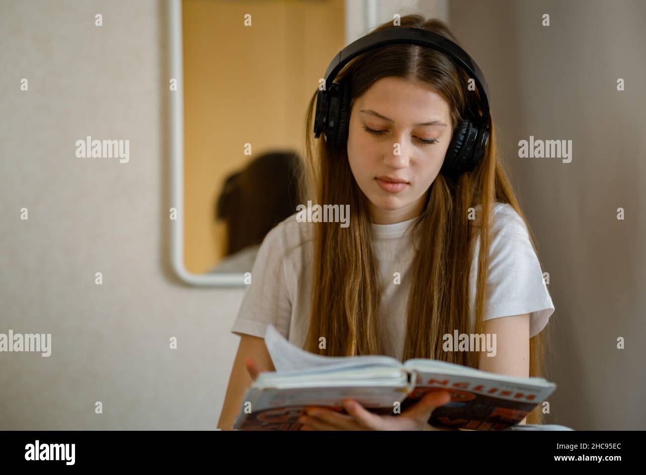 Young teenage girl in headphones with a textbook in her hands. Stock Photo