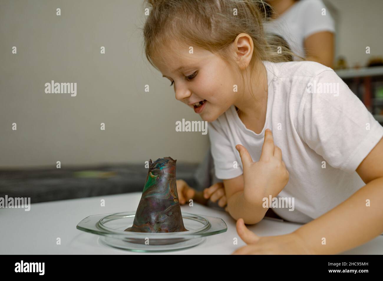 Child girl at home, looking into the mouth of plasticine volcano, curiosity Stock Photo