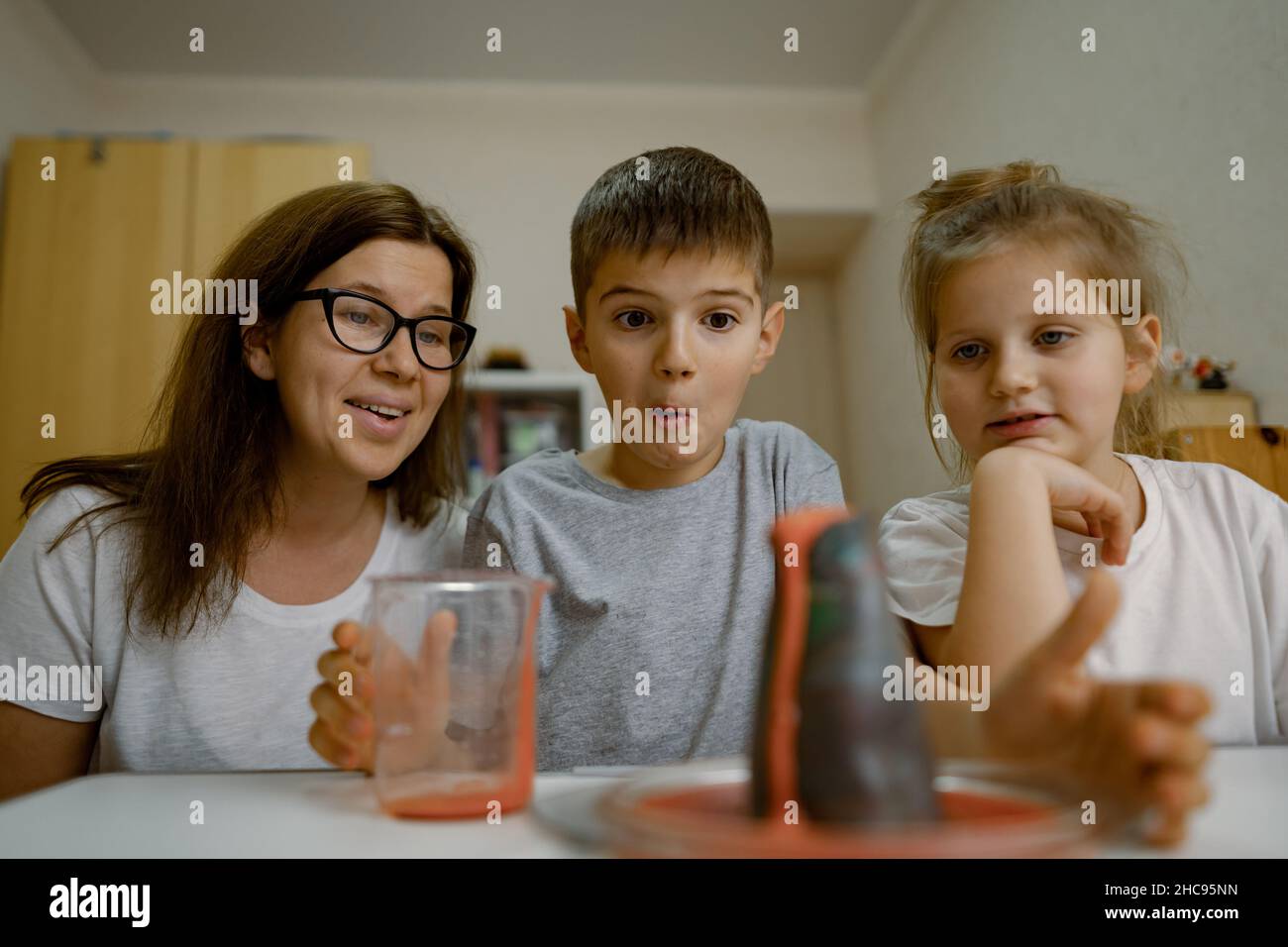 Mom and children at home are conducting an experiment with volcanic eruption. Stock Photo