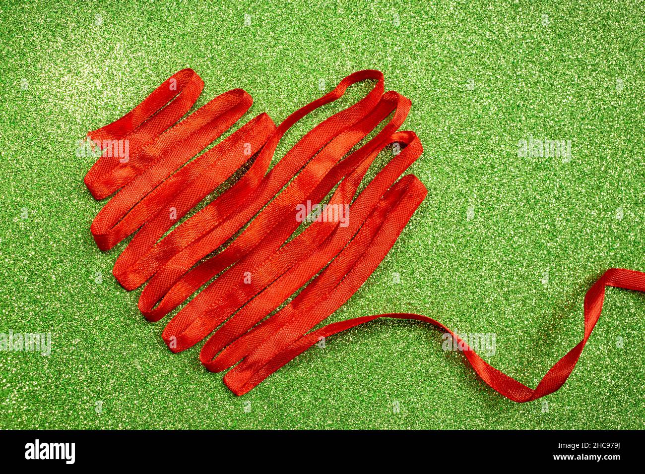 heart shape made of red satin lace, on green glitter background. Satin