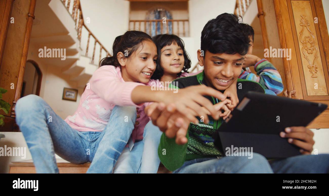 Closeup of four Indian kids sitting on the wooden stairs and playing onthe phone in a house Stock Photo