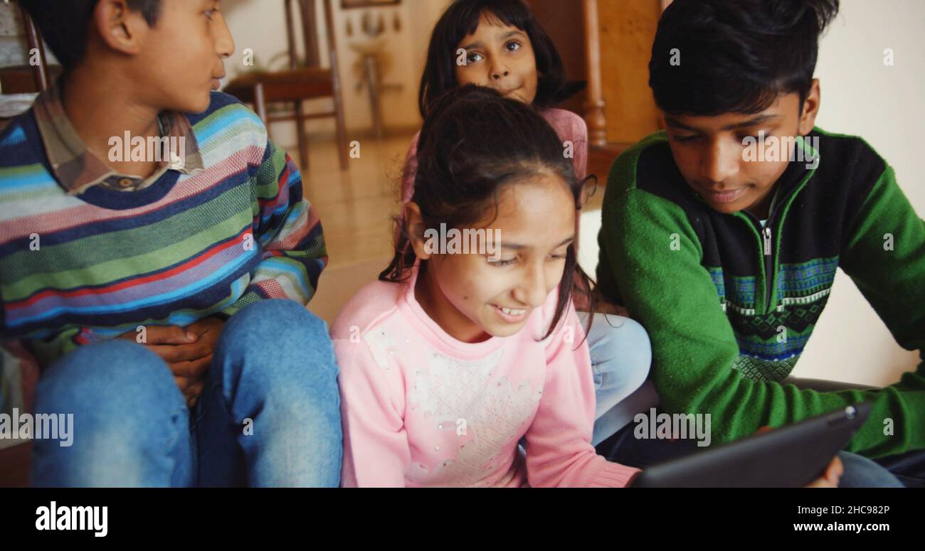 Closeup of four Indian kids sitting on the wooden stairs and playing on the phone in a house Stock Photo