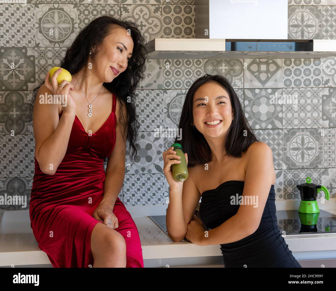 two women enjoying their time having a snack in the kitchen, well-dressed in formal clothes Stock Photo