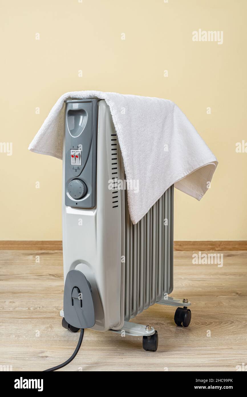 Oil filled electric heater covered with a towel in a room. Terry towel  dries on the portable hot radiator heater at home. Dangerous using of heater  Stock Photo - Alamy