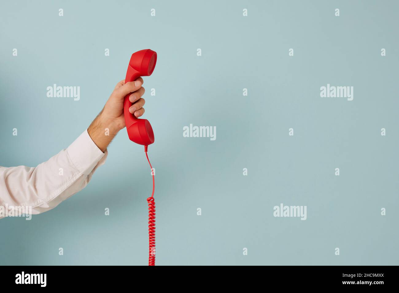 Unidentified man holding red wired retro telephone handset on light blue banner background. Stock Photo