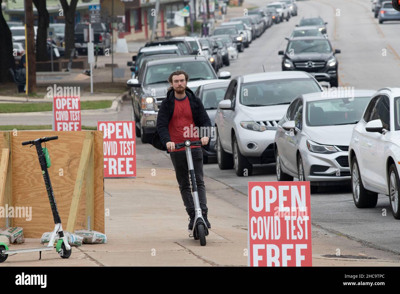 Austin, Texas, USA. 26th December, 2021. A man on a scooter flies past a mobile private COVID testing site overwhelmed by residents wanting to get tested during the holidays. Patrons reported up to two-hour waits at the drive-through site, one of several opened over the Christmas holidays. Credit: Bob Daemmrich/Alamy Live News Stock Photo