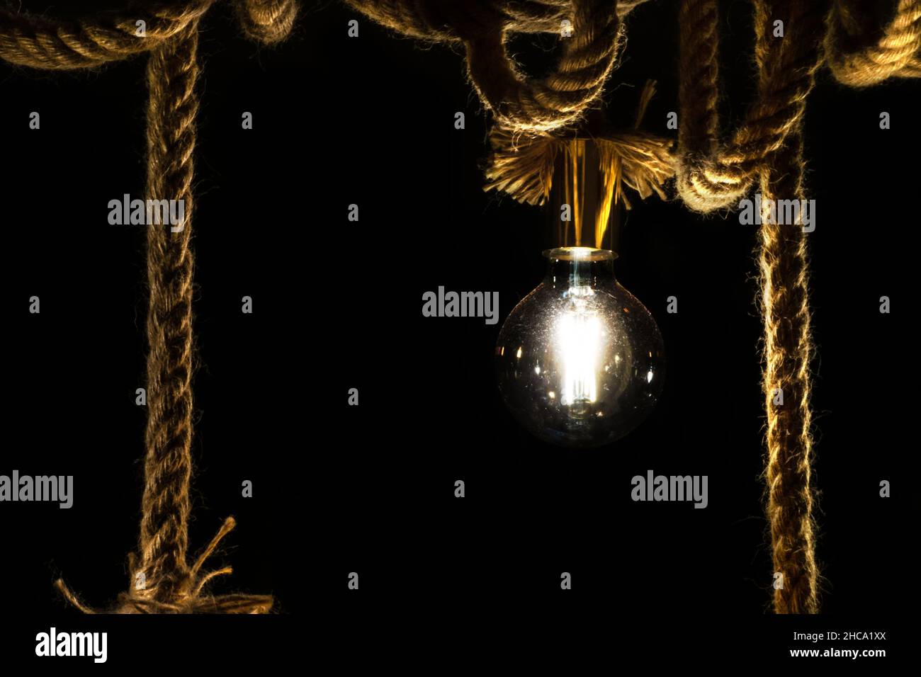 Old light bulb on rope in front of black background Stock Photo
