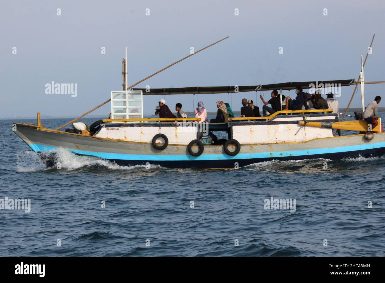 a motorized wooden boat takes its passengers to a small island near the main island of one of the islands in Indonesia Stock Photo