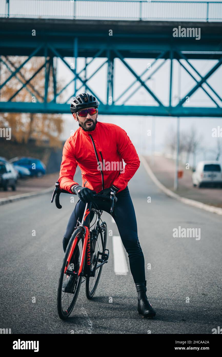 Front view of a young cool male cyclist in red sportswear riding a bicycle on a gloomy day Stock Photo