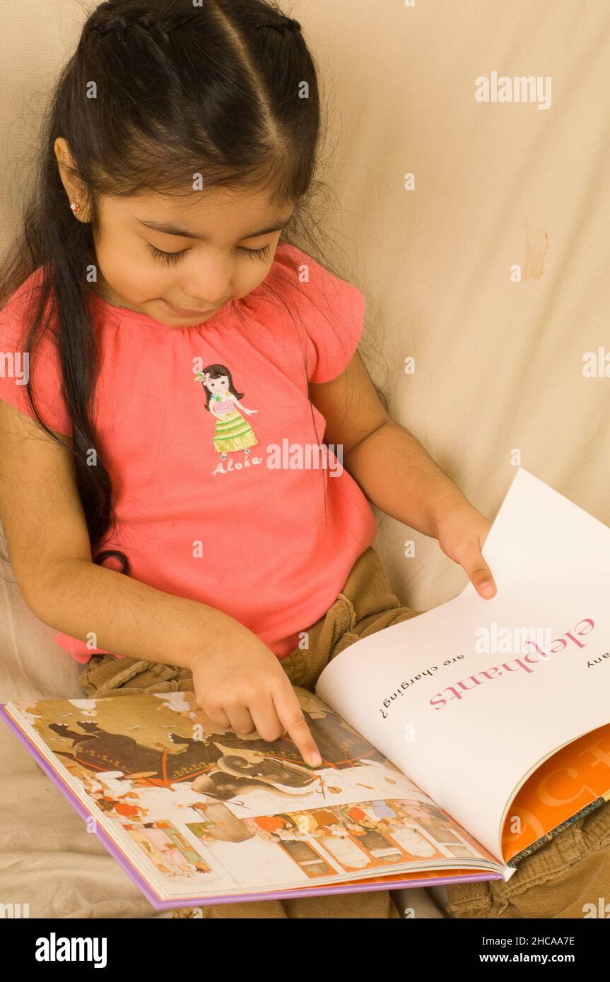 3 year old girl looking at book closeup vertical Mexican American Stock Photo