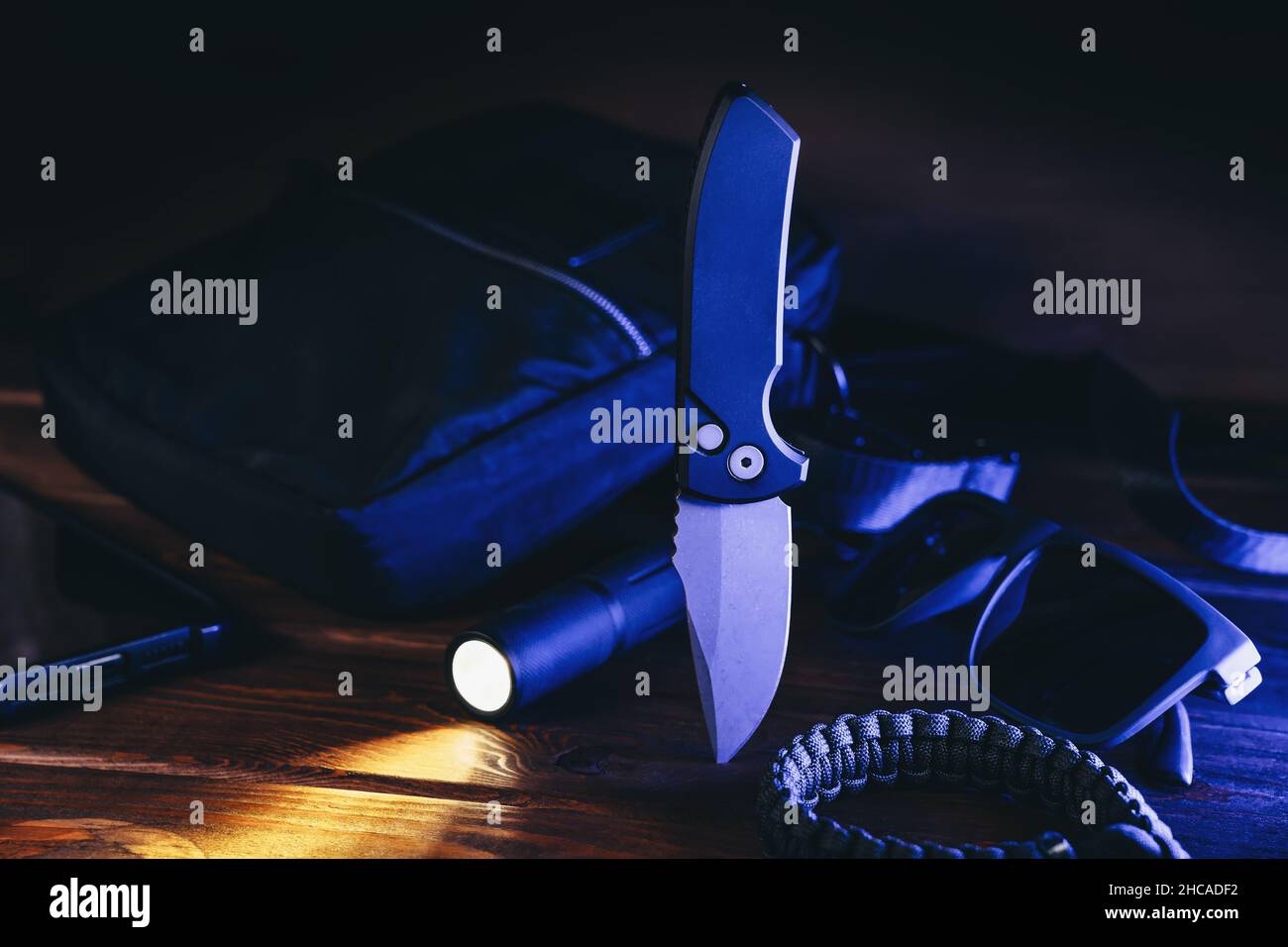 Everyday carry or EDC survival tactical set for modern man in blue light. Pocket automatic knife, flashlight, paracord and bag. Stock Photo