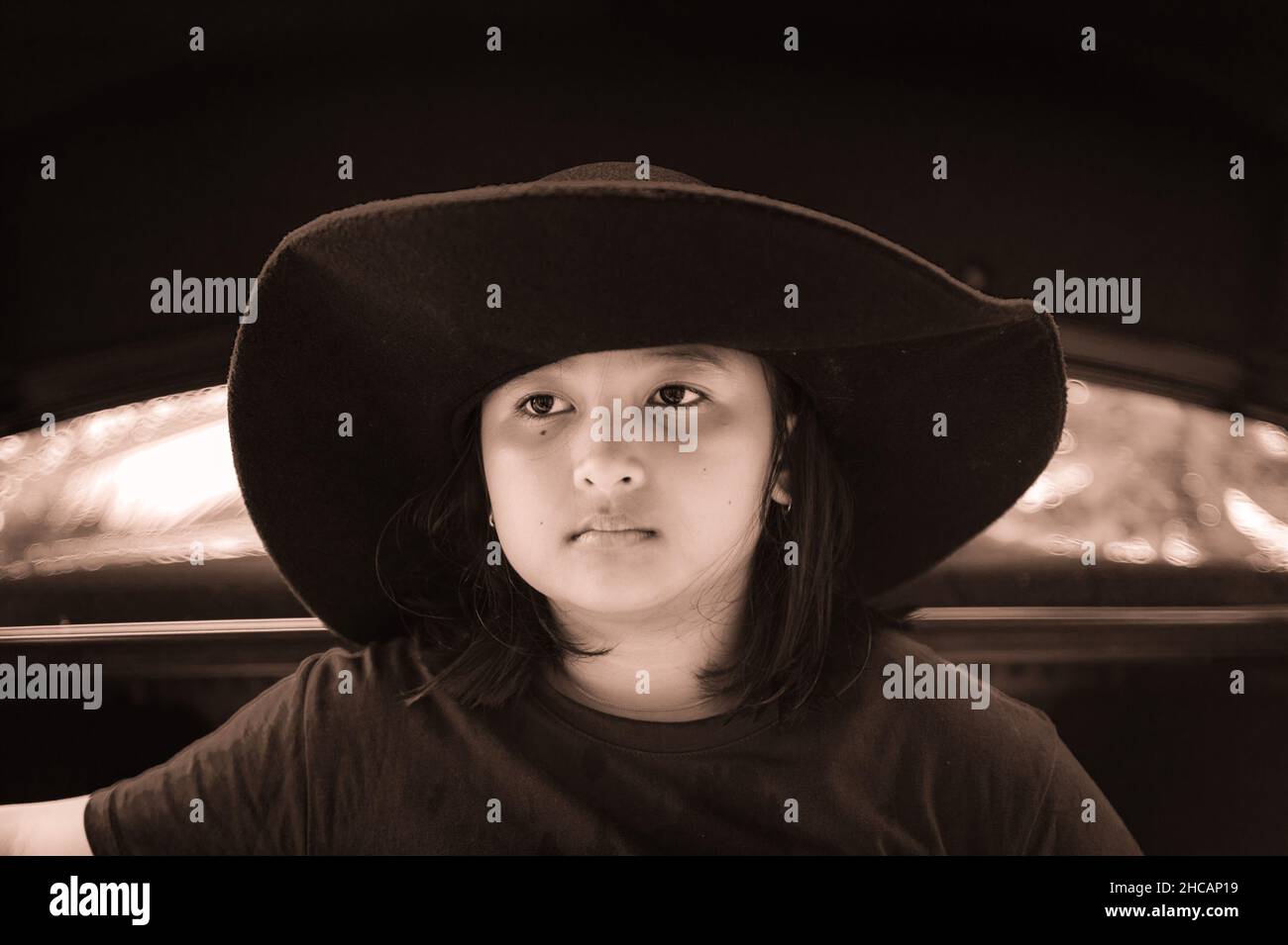 Young girl sitting on black car trunk  wearing black hat and black t shirt. Stock Photo