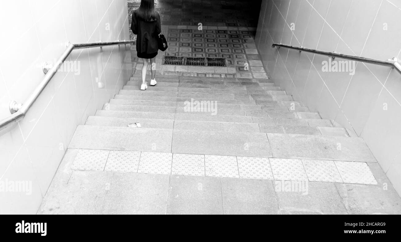 A woman, seen from behind walking down the stairs to enter the passage. concept: alone, walking down, danger, book or album cover Stock Photo