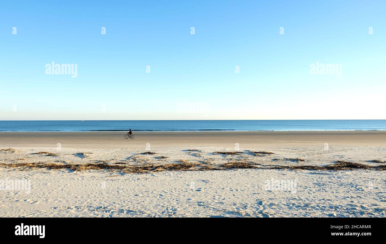 A single bike rider on a lonely stretch of clear sandy beach in Hilton Head, South Carolina, USA; fun, exercise and relaxation on a sunny day. Stock Photo