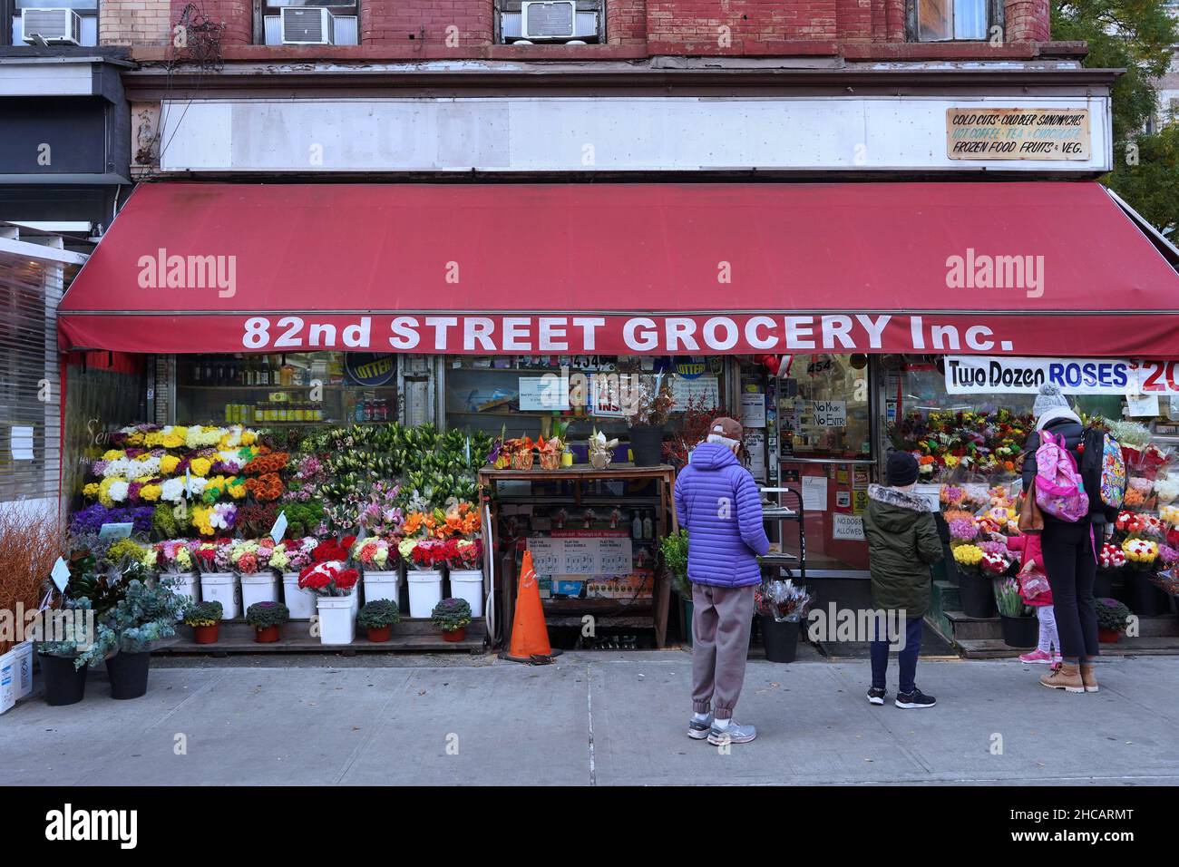 New York, NY - November 15, 2021:  Shoppers outside an old fashioned local grocery store with colorful outdoor display of flowers Stock Photo