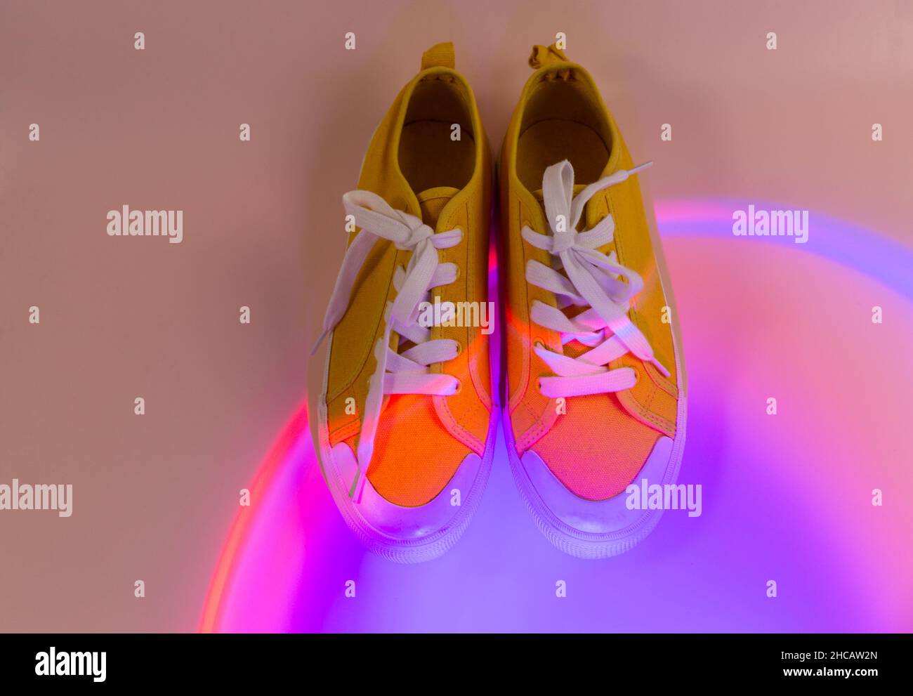 Trendy fashion white sneakers on geometry podium on abstract bright background. Neon lights on casual shoes. Violet and orange gradient light. Stock Photo