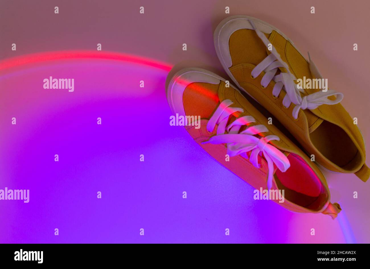 Trendy fashion white sneakers on geometry podium on abstract bright background. Neon lights on casual shoes. Violet and orange gradient light. Stock Photo