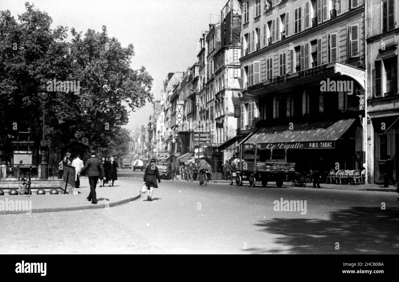 Place Pigalle Metro entry and Boulevard de Clichy, April 1945. The main view looks west on the boulevard where there are pedestrians; a cart of lumber drawn by a horse, and a few vehicles. southwest across a nearly empty square towards the Folies Pigalle and down Rue Jean-Baptiste Pigalle. The image contains signage and advertisements including Cine Vox and Le Pigalle. Stock Photo