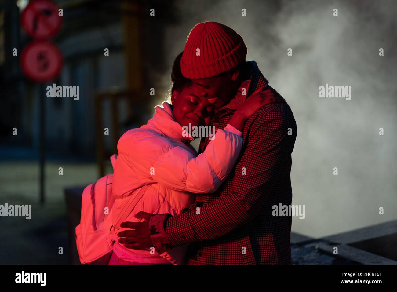 Young happy romantic african couple in love hugging outdoors at night, standing on empty dark street Stock Photo