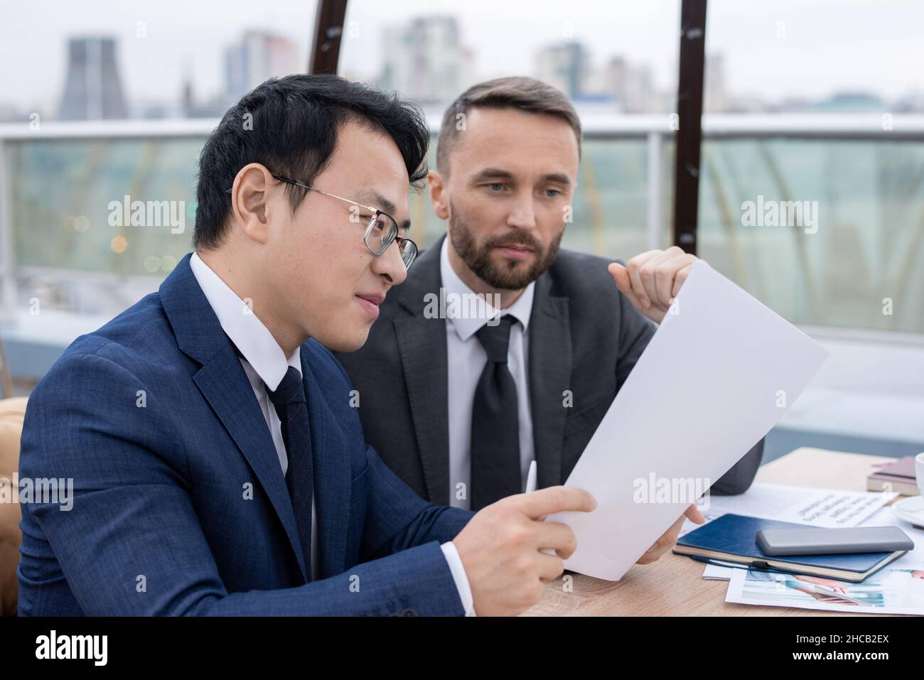 Young Chinese broker showing his Caucasian colleague new contract