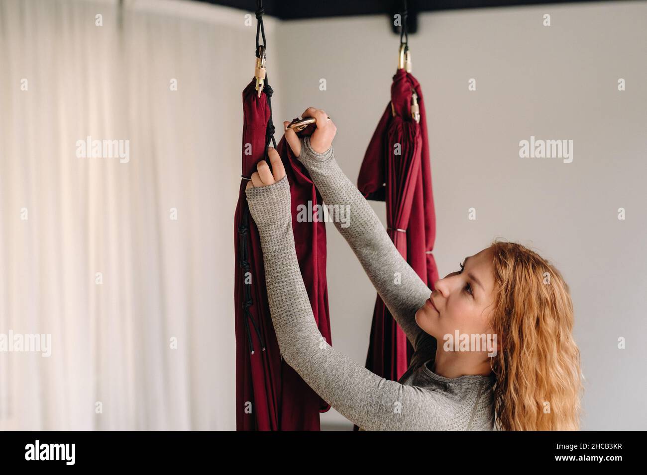 A woman fastens a hook from a hanging hammock for yoga in the gym. Stock Photo