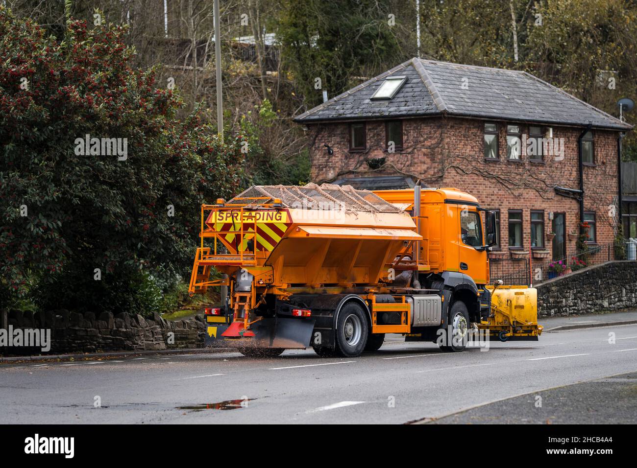 Orange winter maintenance gritter salt spreading lorry with snow plough fitted treating road surface before freezing temperatures to prevent ice form Stock Photo