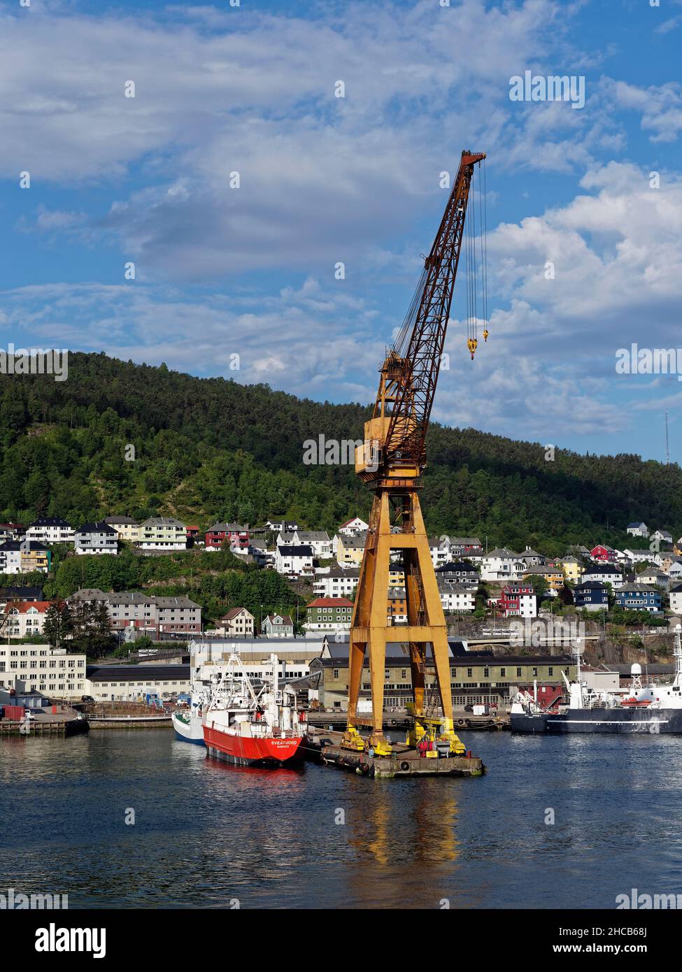 Fishing Vessels moored beside a large Yellow Shore Crane at the Fishing Port in Bergen, with traditional stone warehousing in the background. Stock Photo