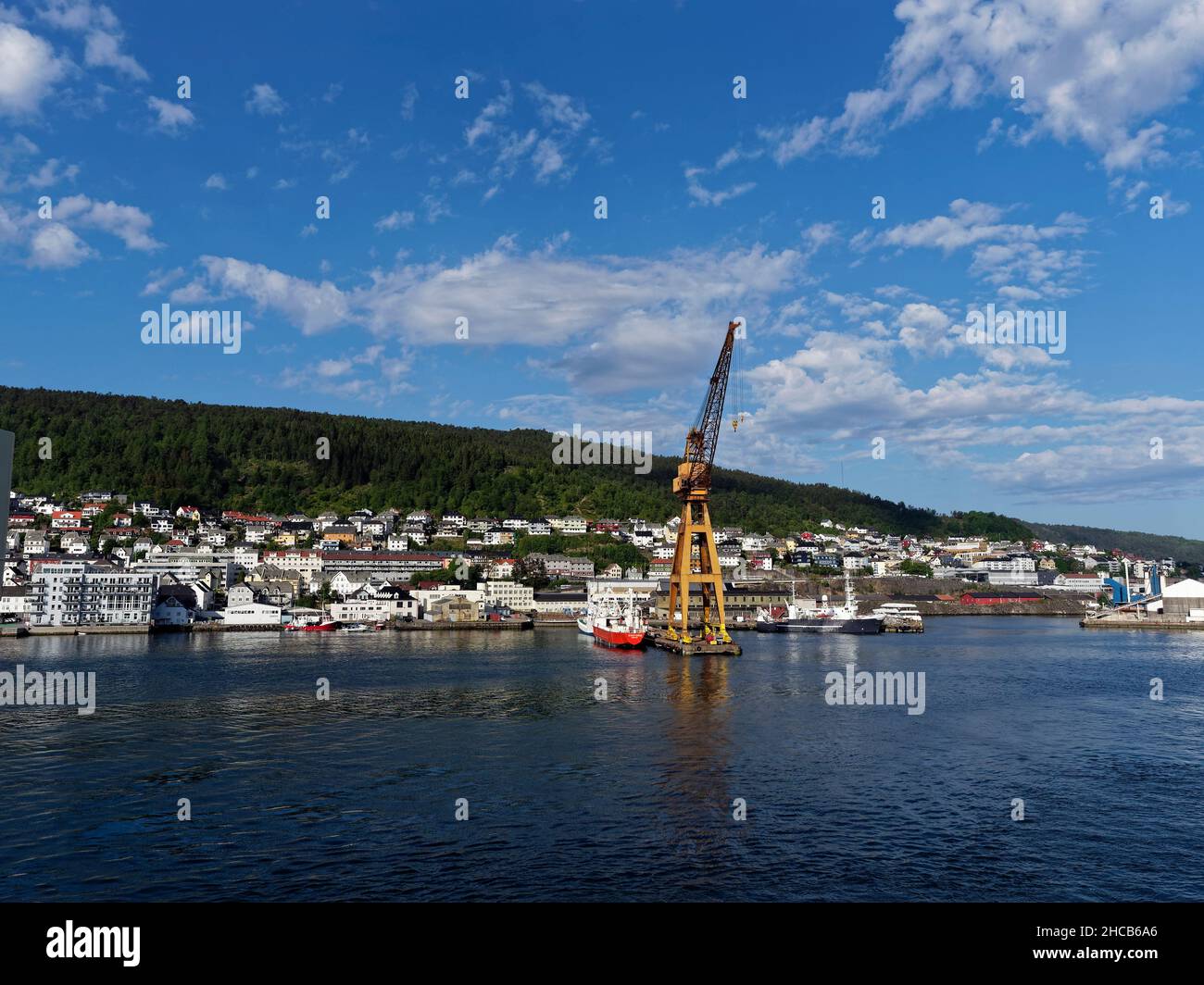Fishing Vessels moored beside a large Yellow Shore Crane at the Fishing Port in Bergen, with apartments and houses at the waterfront. Stock Photo