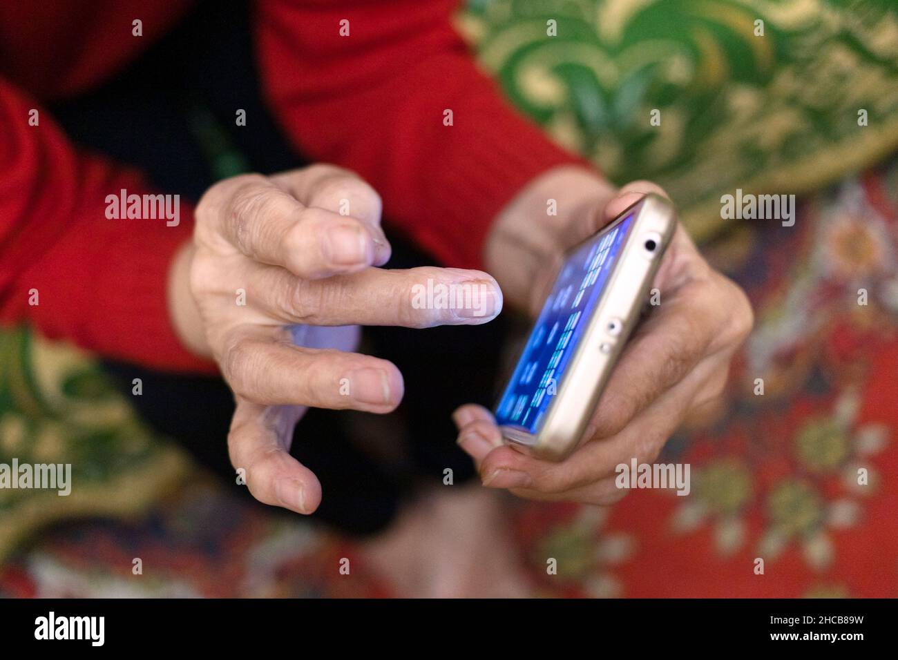 above view of hand of aged woman playing on smartphone in evening in village house (focus on the middle finger) Stock Photo