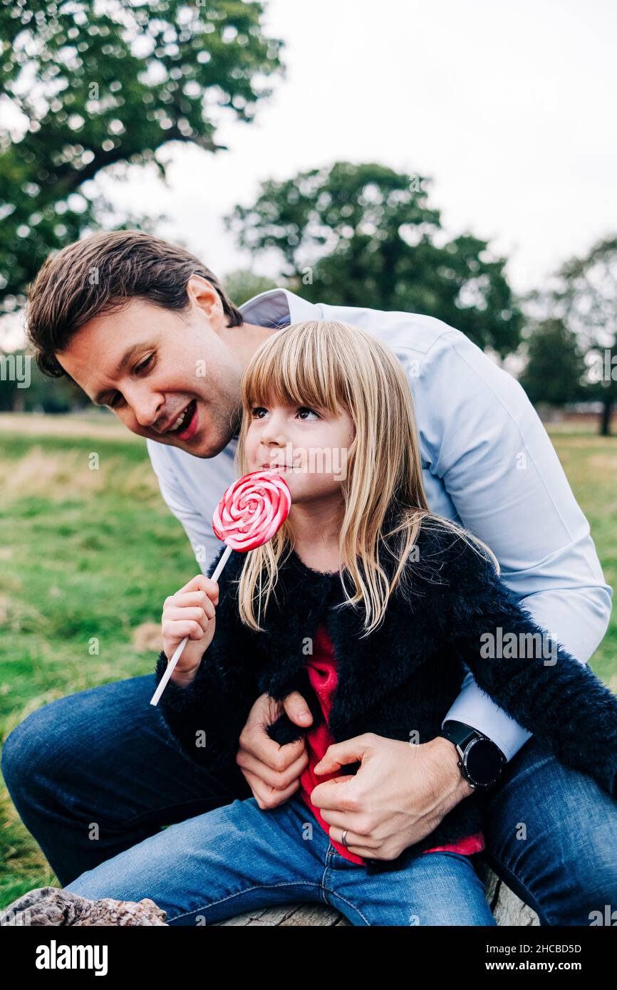 Father looking at daughter eating lollipop in park Stock Photo