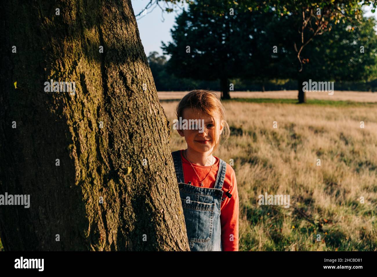 Cute girl standing by tree in park Stock Photo - Alamy