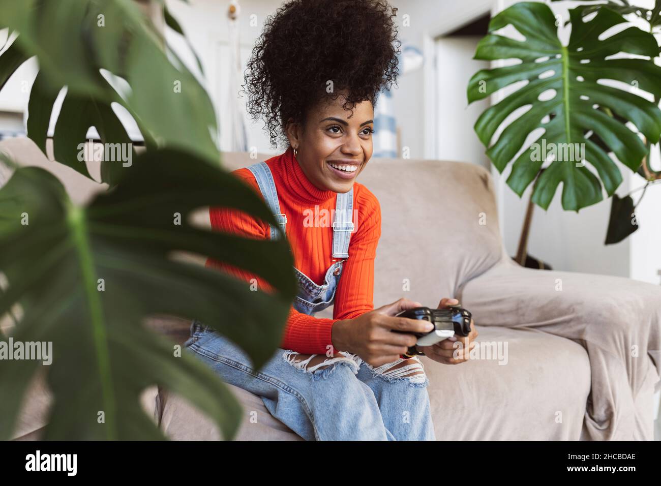 Happy curly haired woman playing video game on sofa Stock Photo