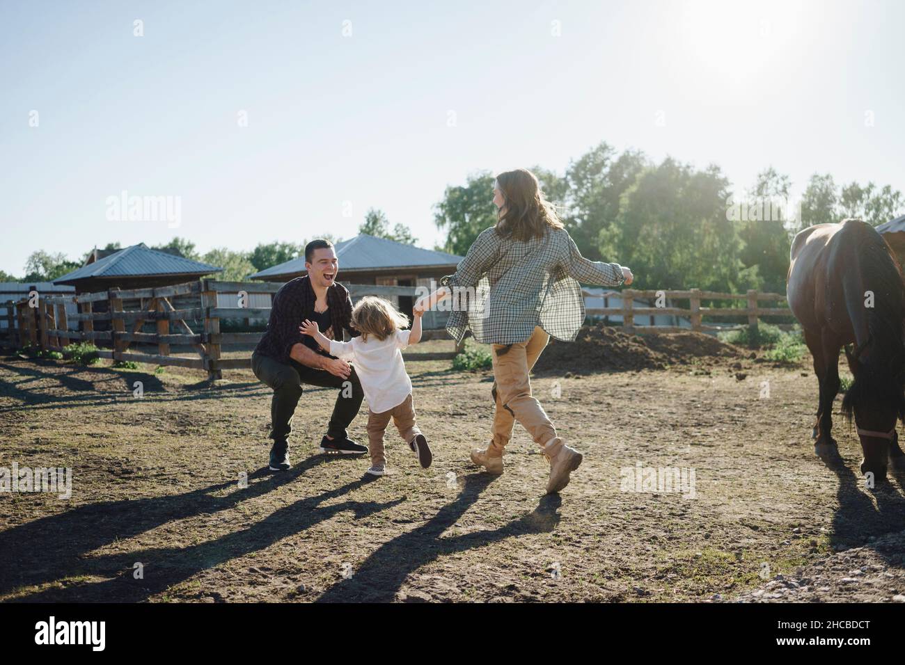 Mother and daughter running towards father at horse farm on sunny day Stock Photo