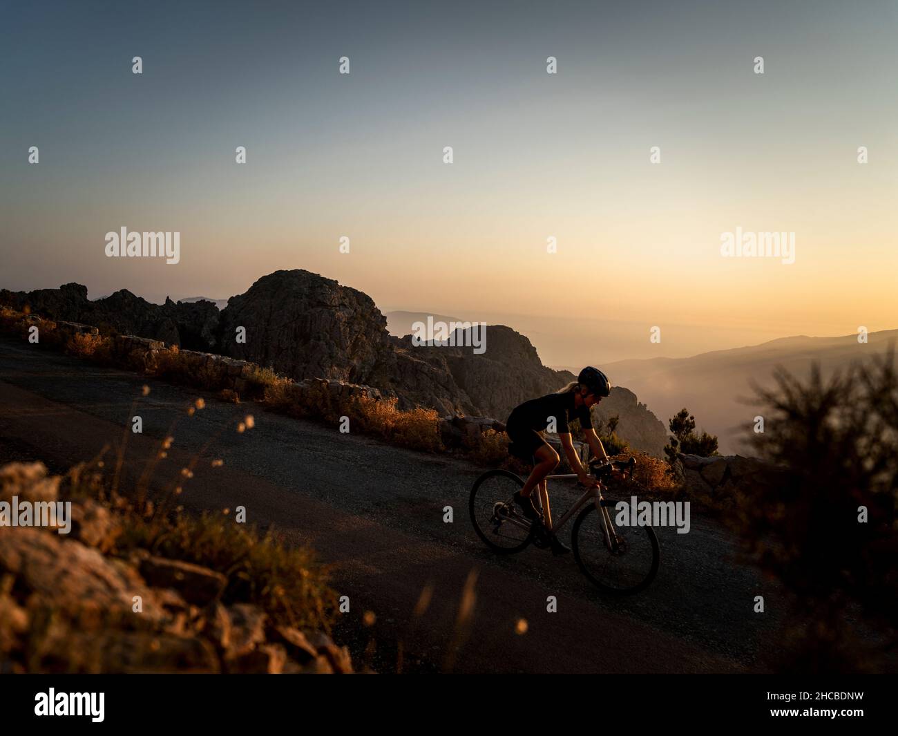 Athlete cycling on mountain road at sunset Stock Photo