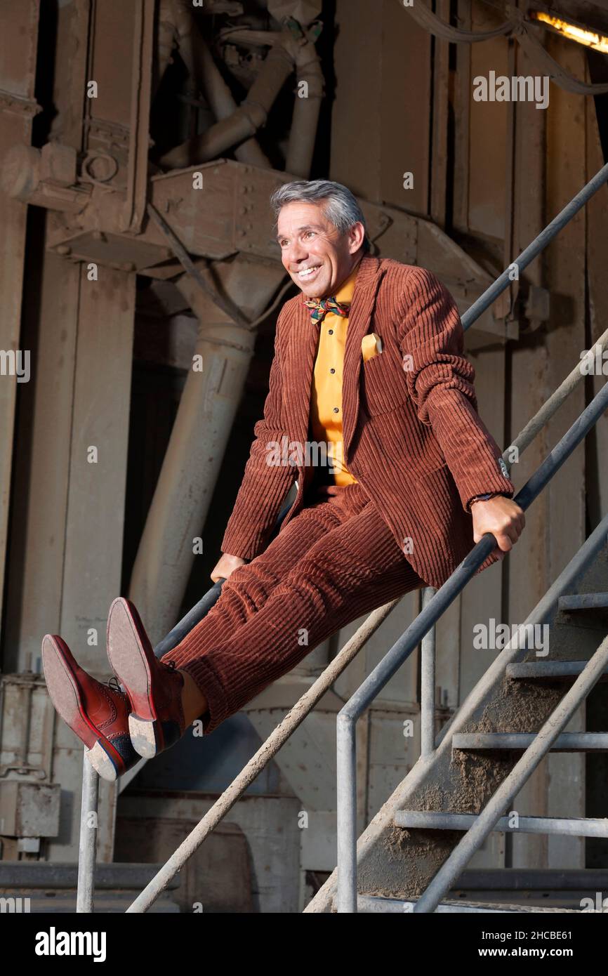 Playful man in full suit balancing on staircase railing Stock Photo