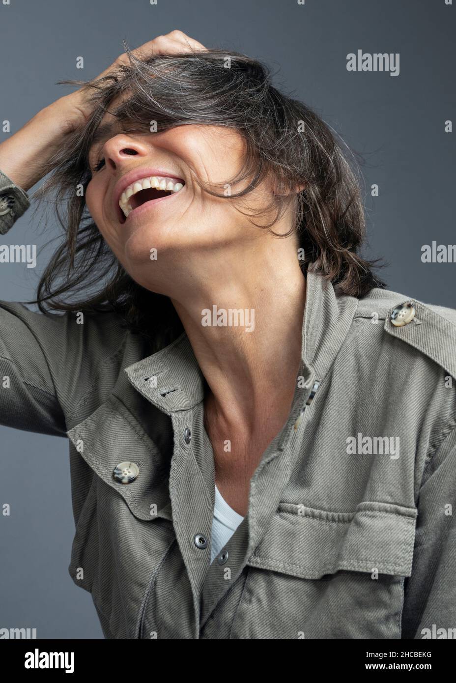 Smiling woman with hand in hair against gray background Stock Photo