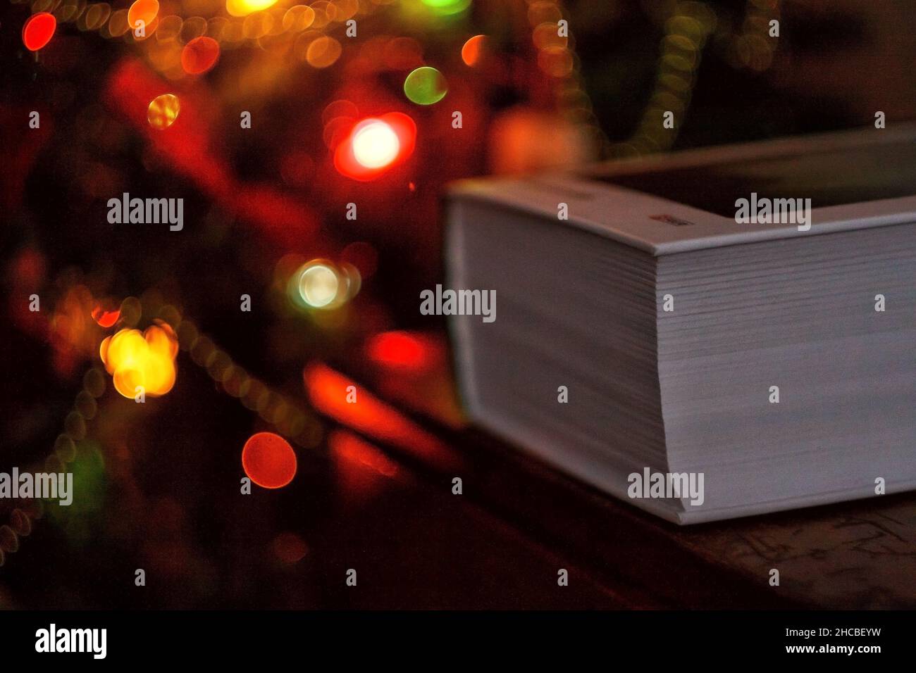 thick book on the background of a christmas tree with christmas lights. Stock Photo