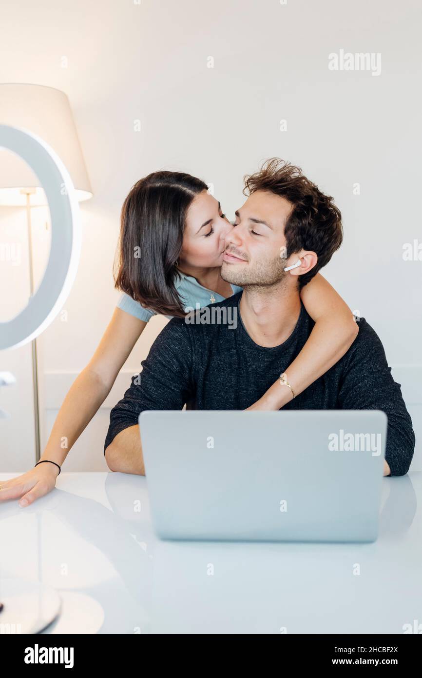 Young woman kissing boyfriend while working in home office Stock Photo