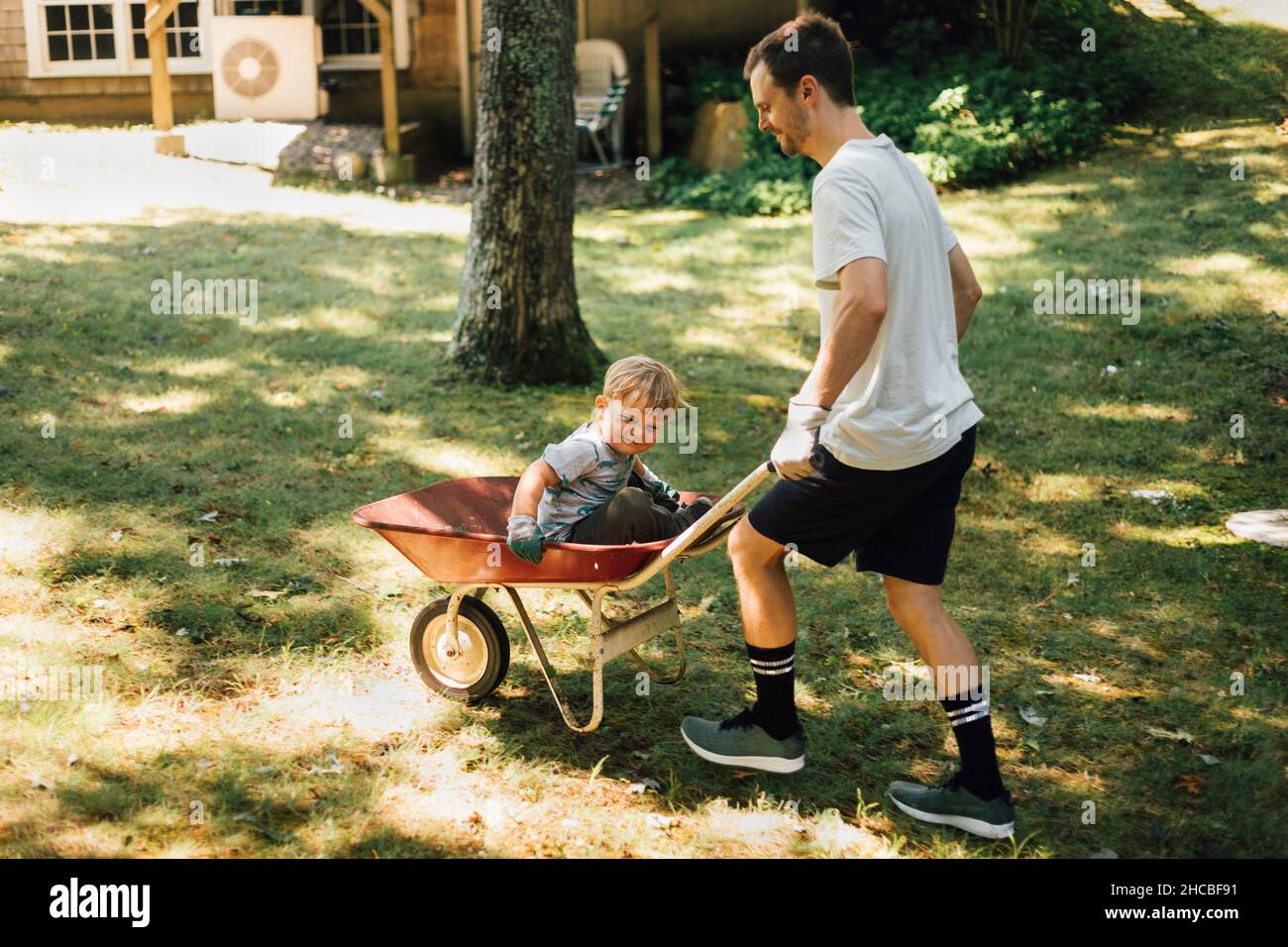 Father pushing son sitting on wheelbarrow Stock Photo