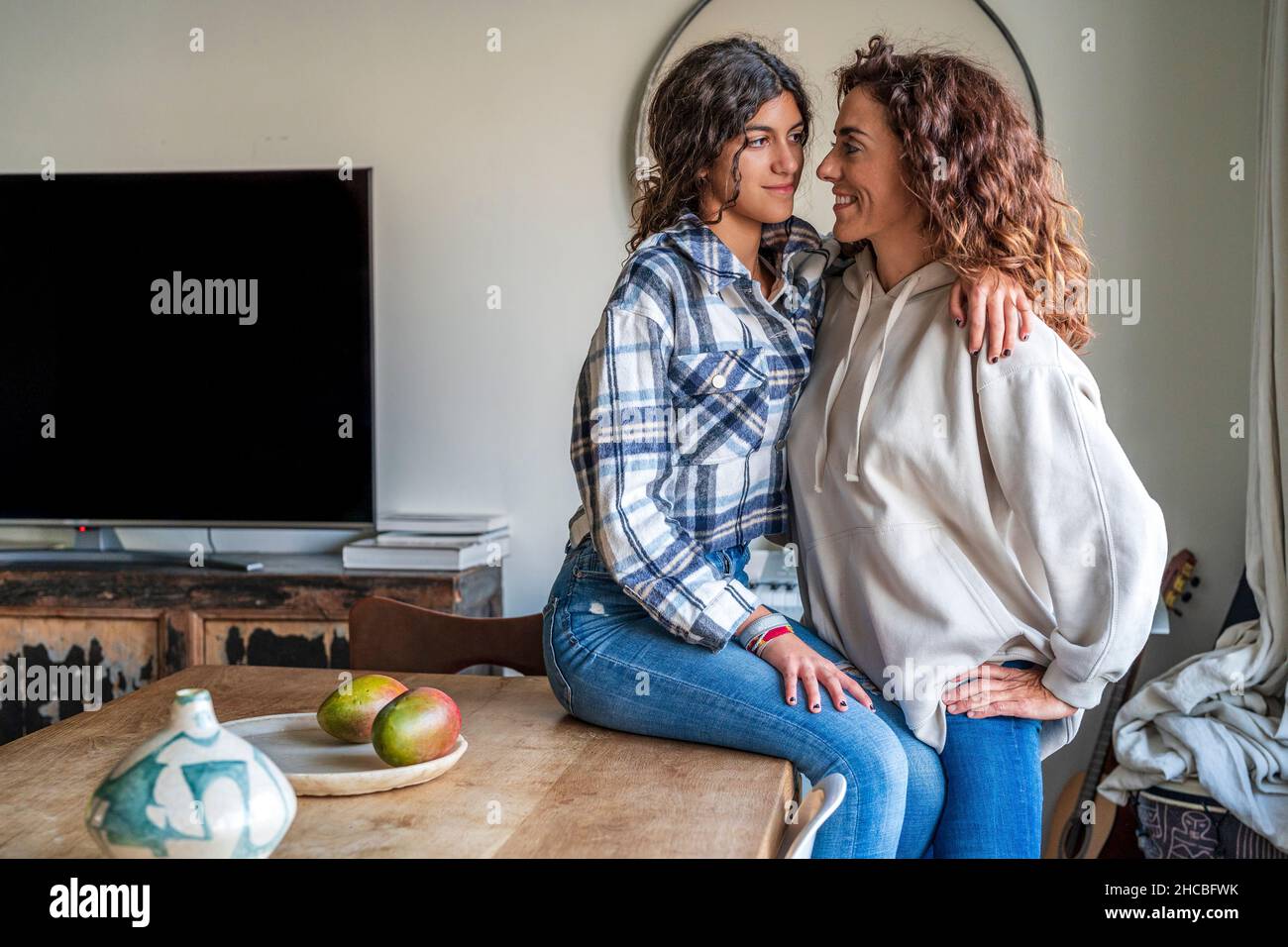 Happy mother looking at daughter sitting on dining table at home Stock Photo