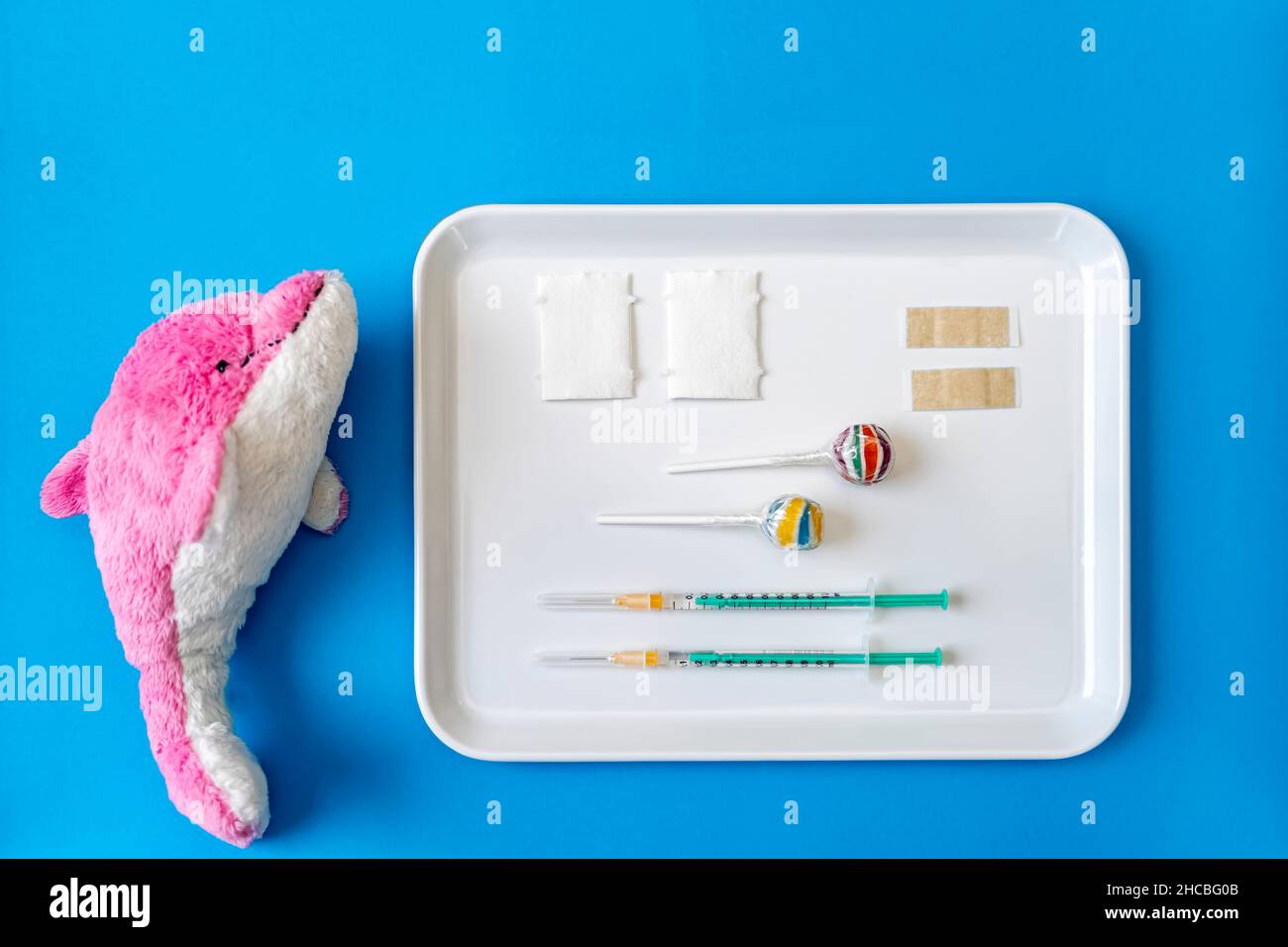 Stuffed dolphin toy by tray of vaccine injections and lollipop on blue background Stock Photo