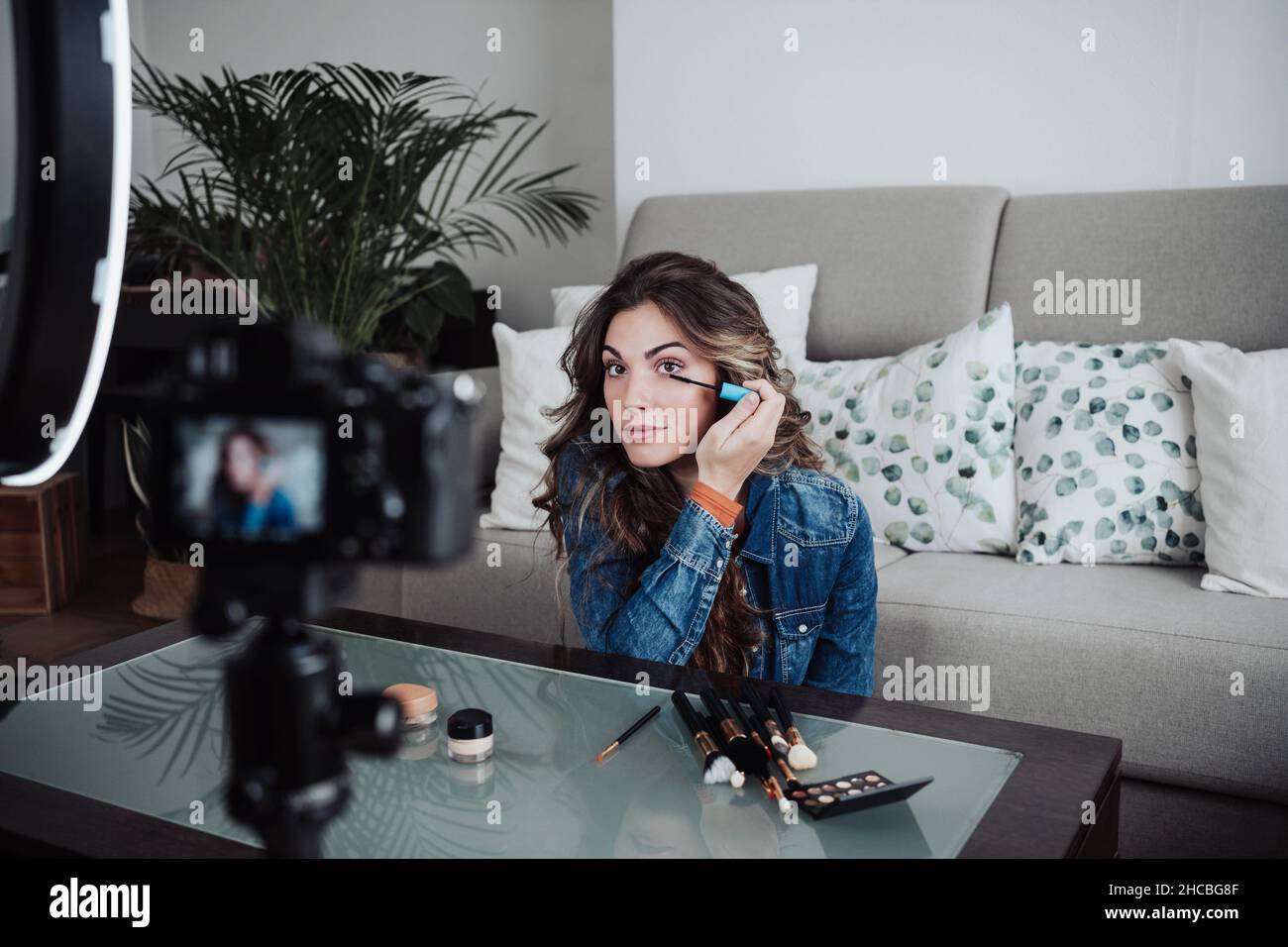 Vlogger applying mascara and filming through home video camera at table Stock Photo