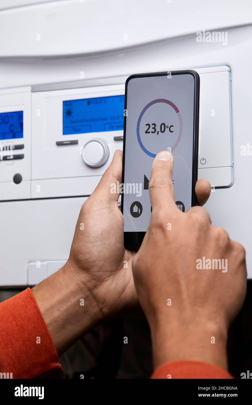 Man adjusting boiler temperature through mobile phone at home Stock
