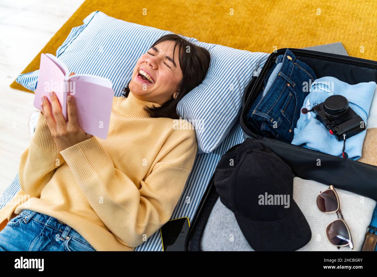Smiling woman taking selfie with smart phone while lying by luggage on bed Stock Photo