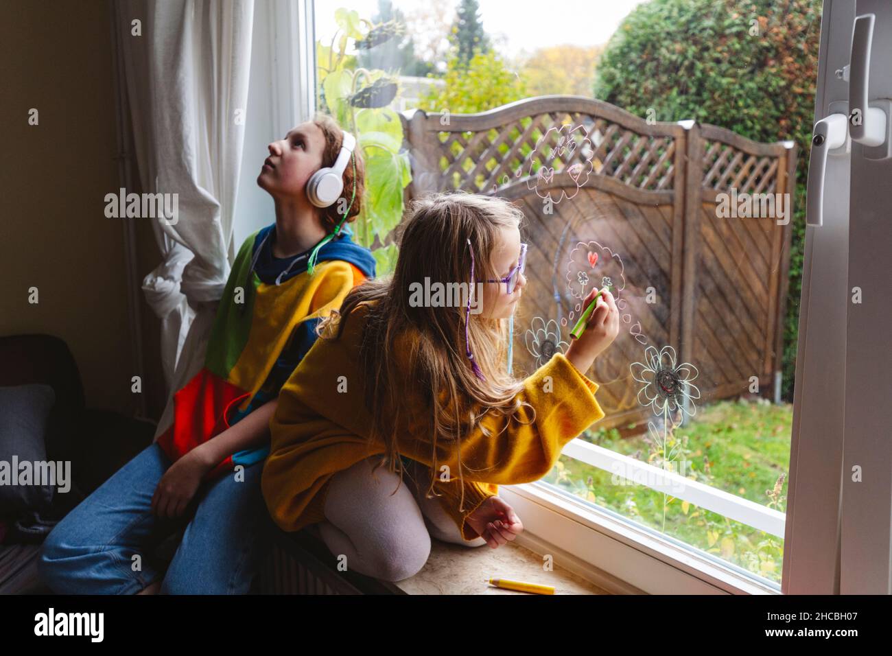 Smiling grandmother standing by granddaughter drawing heart shape on window Stock Photo