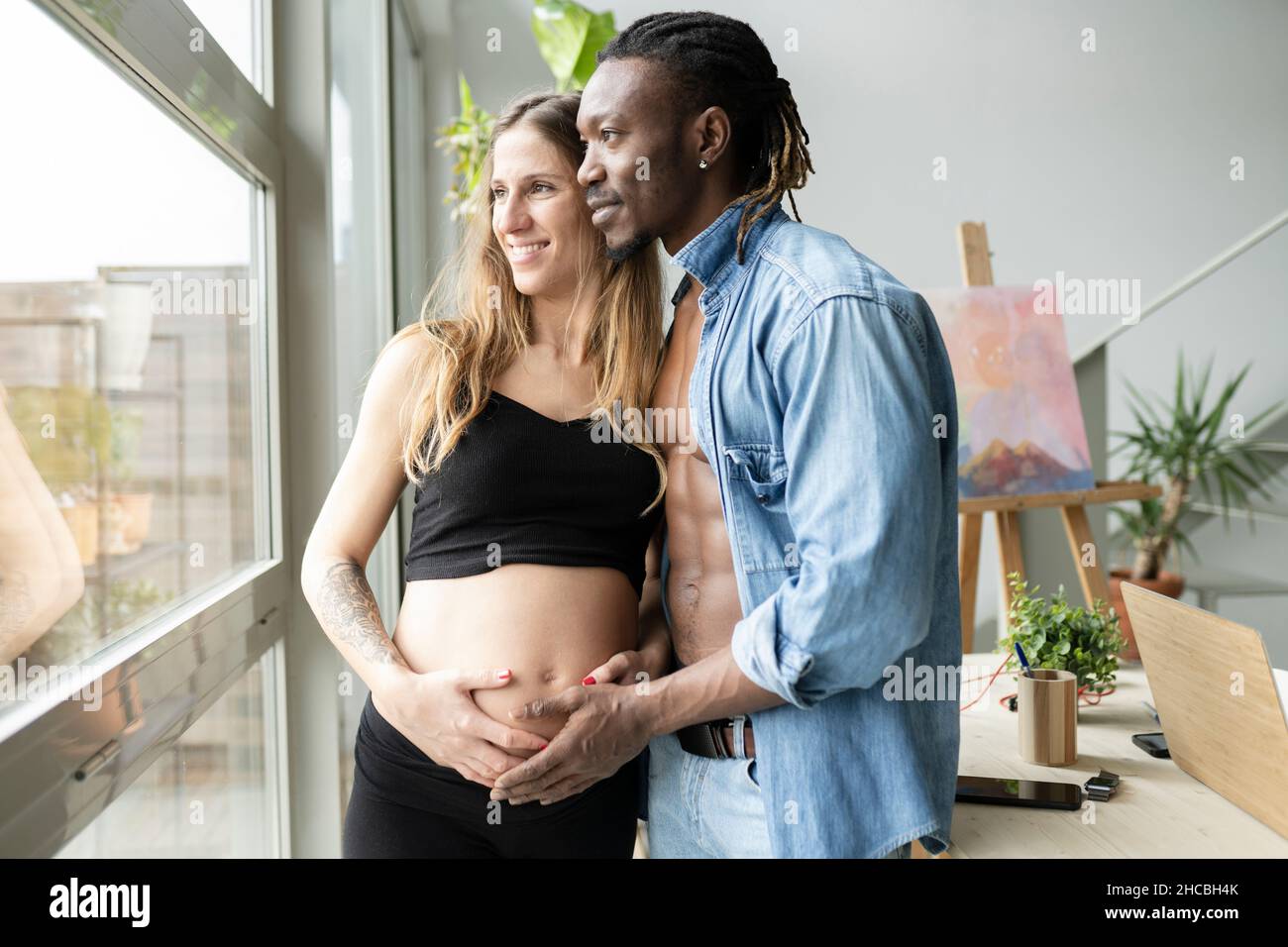 Happy couple expecting baby looking at belly of pregnant woman at home Stock Photo