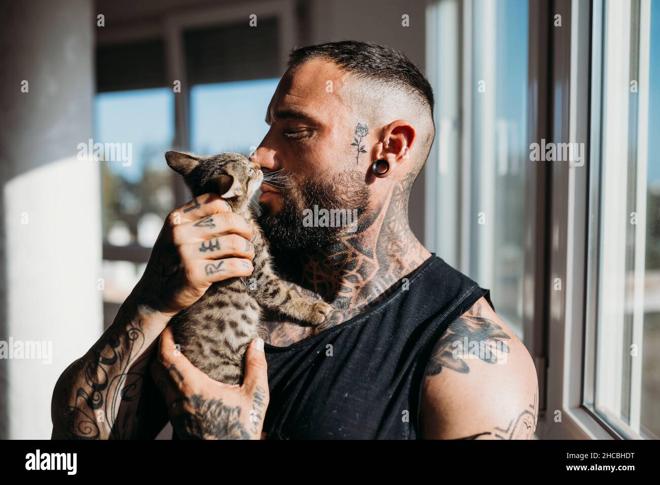 Man with tattoo kissing cat at home Stock Photo