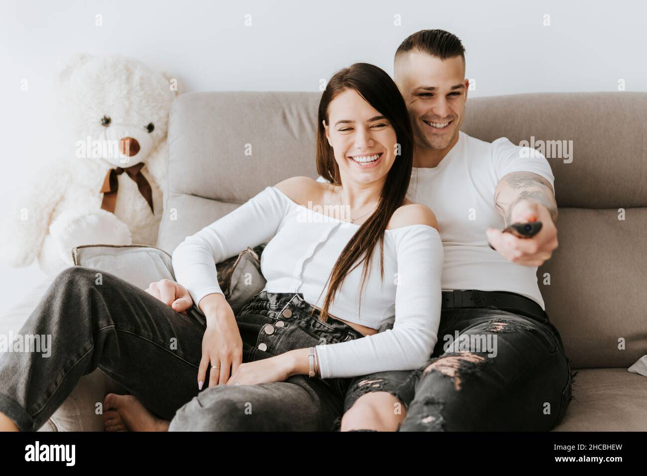 Smiling man holding remote watching TV with woman on sofa Stock Photo