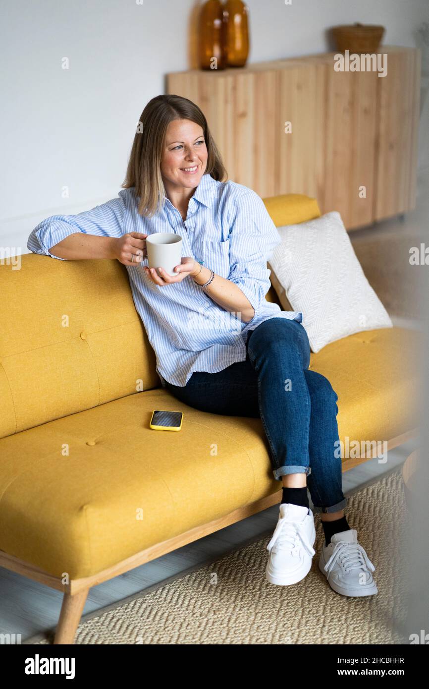 Woman holding mobile phone and sitting with legs crossed at knee on sofa Stock Photo